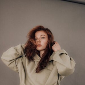 Attractive young female model touching hood of beige hoodie